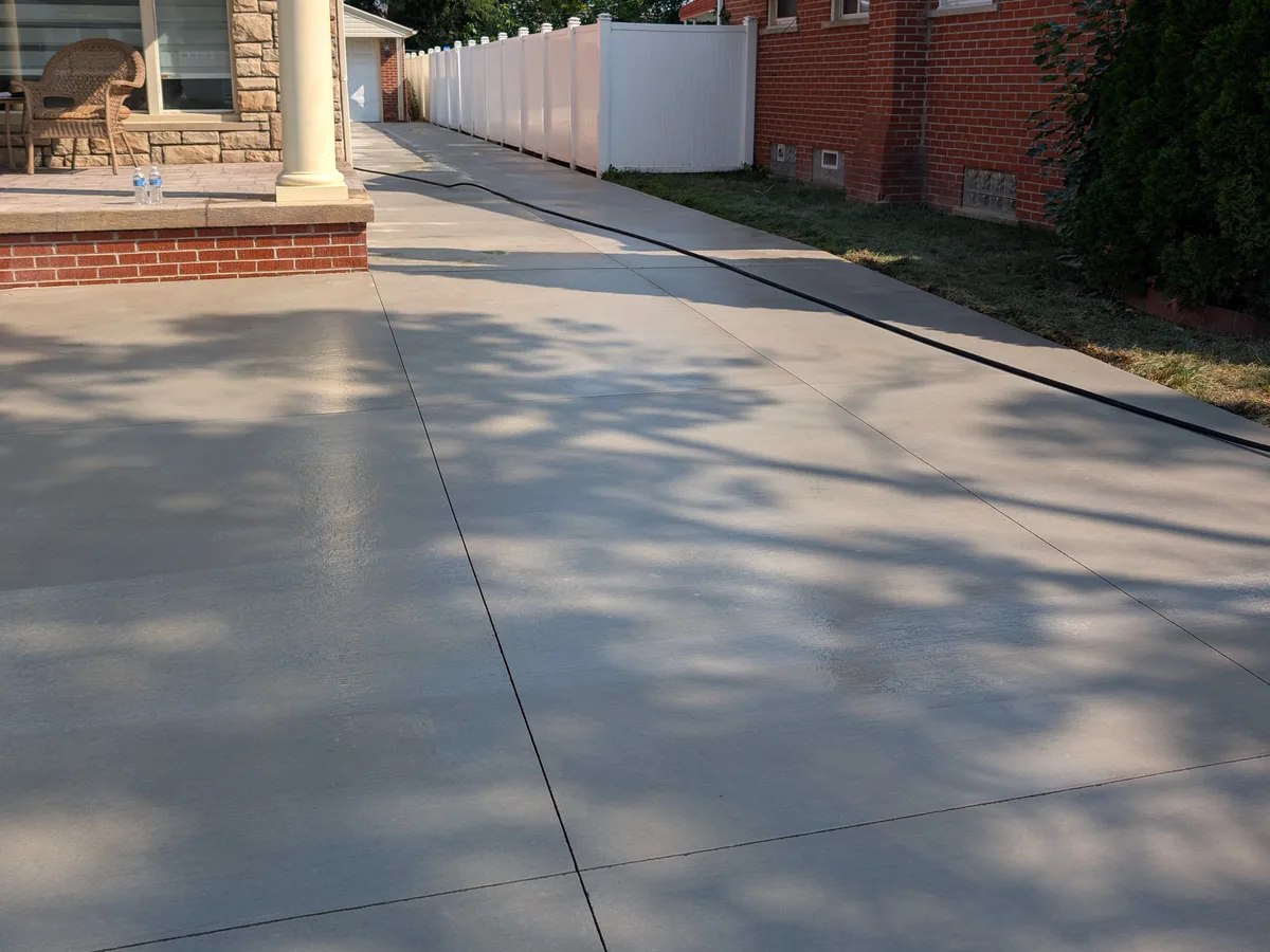 Wide broom-finish concrete driveway running alongside a brick home to a detached garage, Dearborn Heights MI